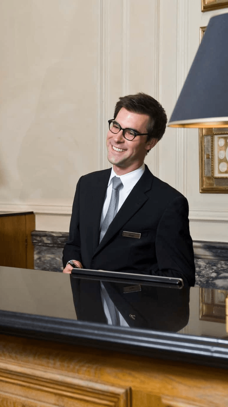 Smiling concierge in a dark suit at a hotel front desk
