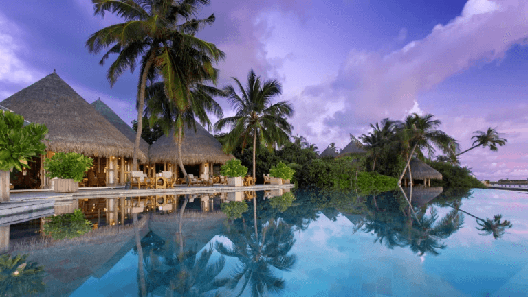 Thatched pavilions and palms reflected in an infinity pool at dusk