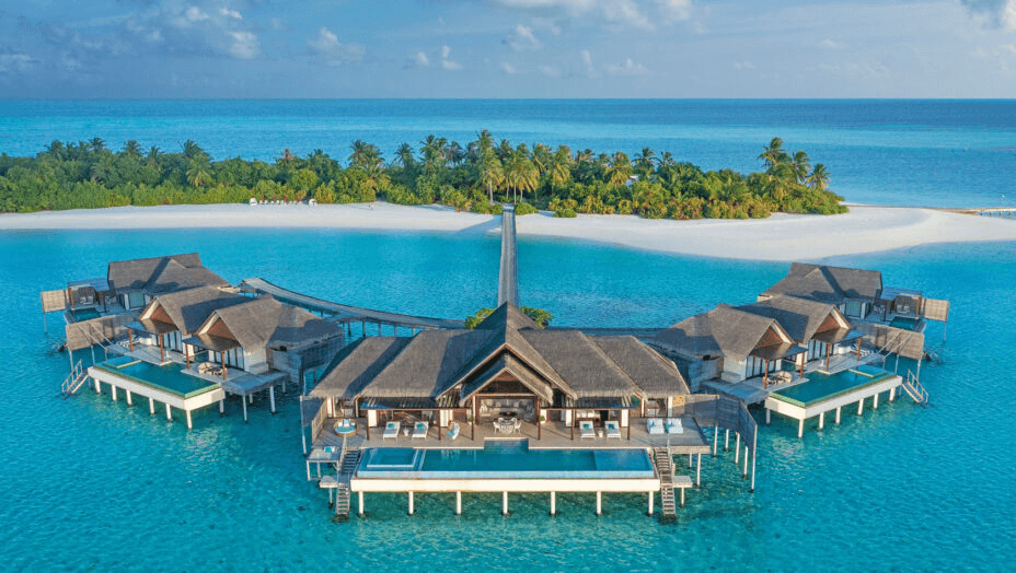 Overwater pavilion and pool villas in front of a palm-fringed island