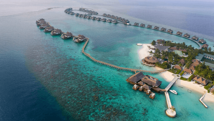 Overwater villas curving out from an island, seen from the air