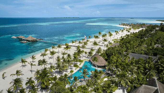 Palm-lined beach and resort pool along a long island, seen from the air