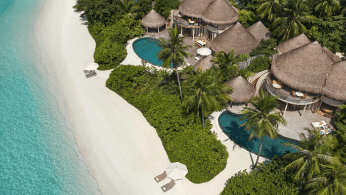 Thatched beach houses and pools beside a white beach, seen from above