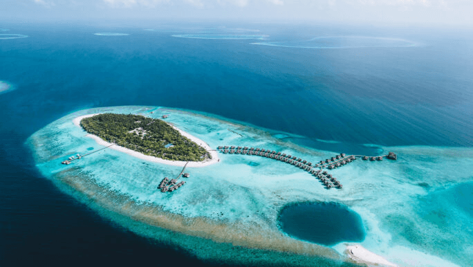 Island resort and overwater villas on a turquoise reef, seen from the air