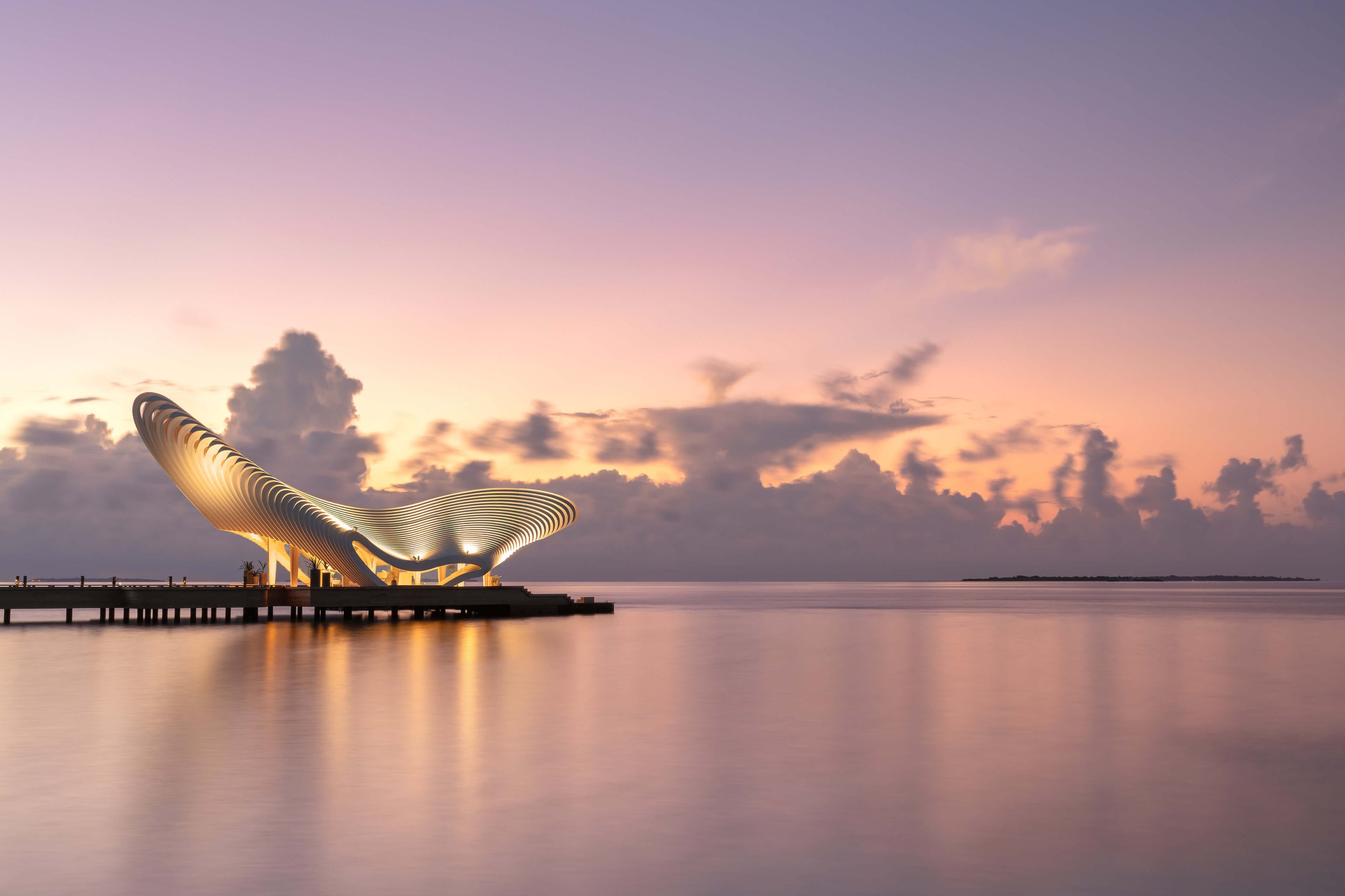 Sculptural white pavilion on a jetty over a calm sea at dusk
