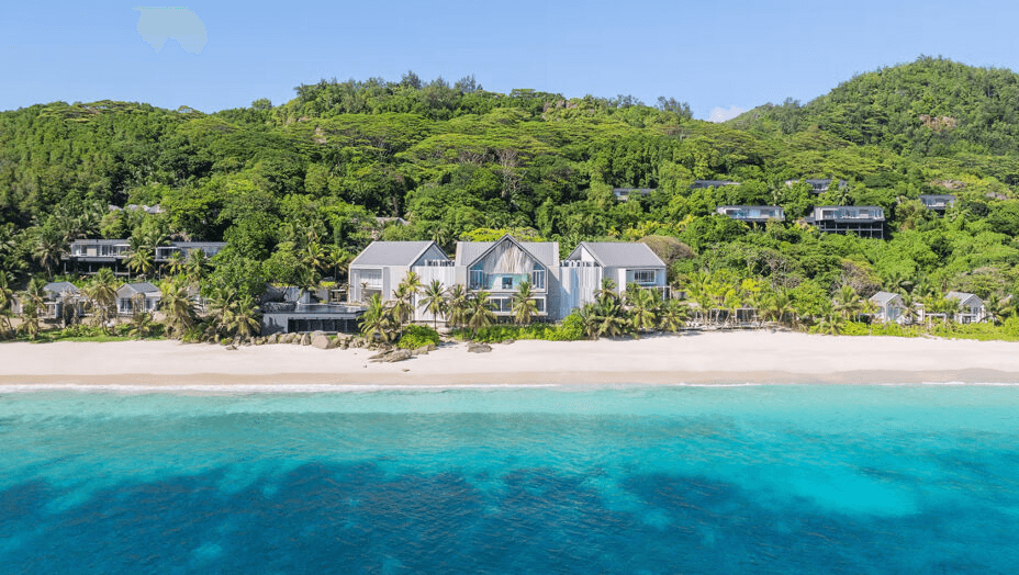Beachfront villas below forested hills, seen from the sea