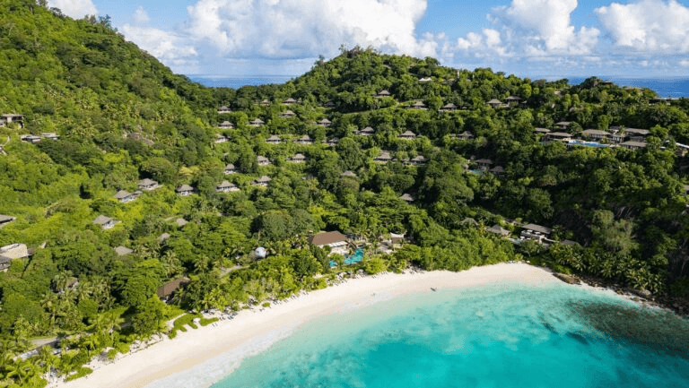 Villas on a forested hillside above a curved white beach