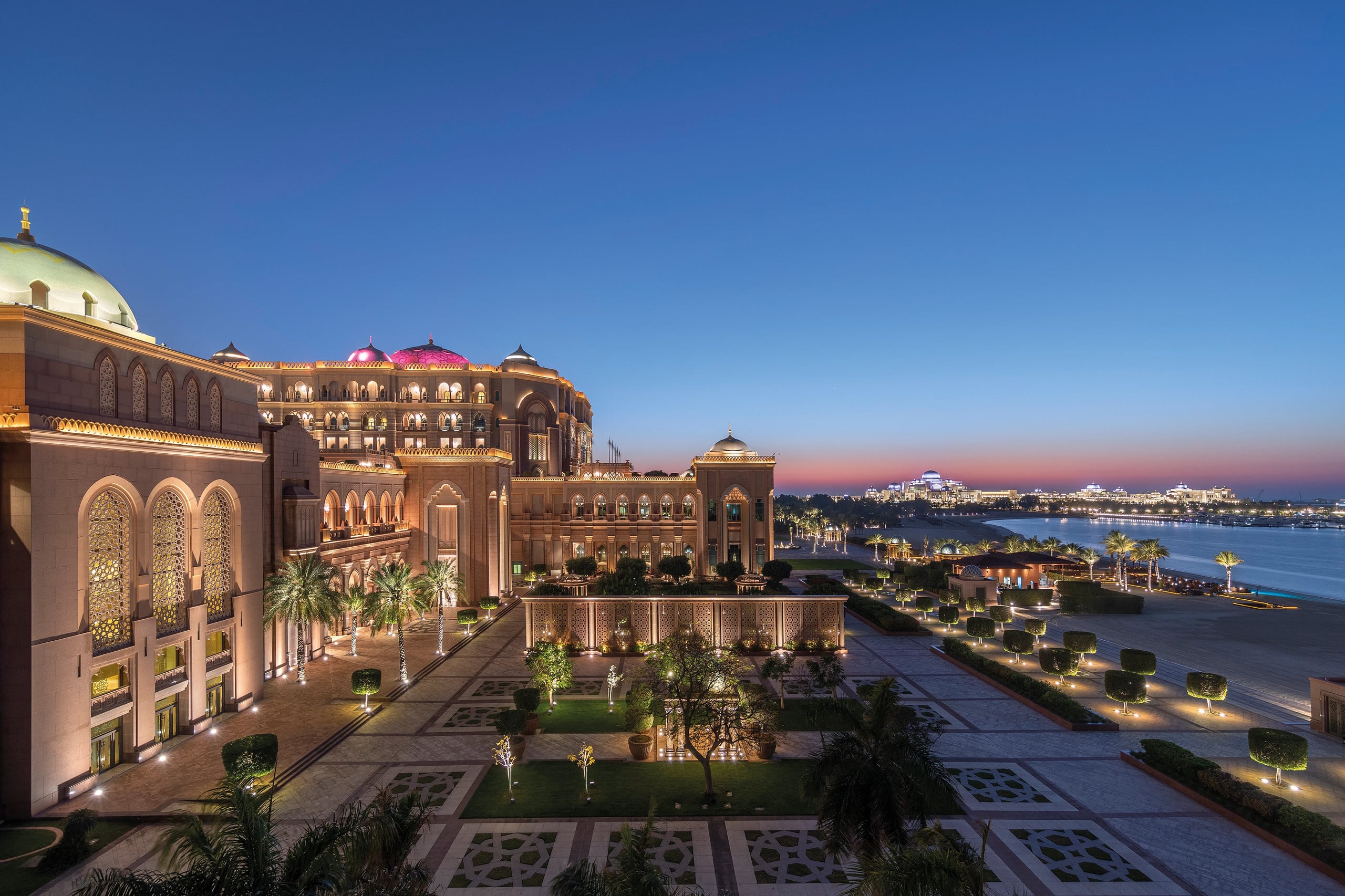 Emirates Palace lit up at dusk above its gardens and beach in Abu Dhabi