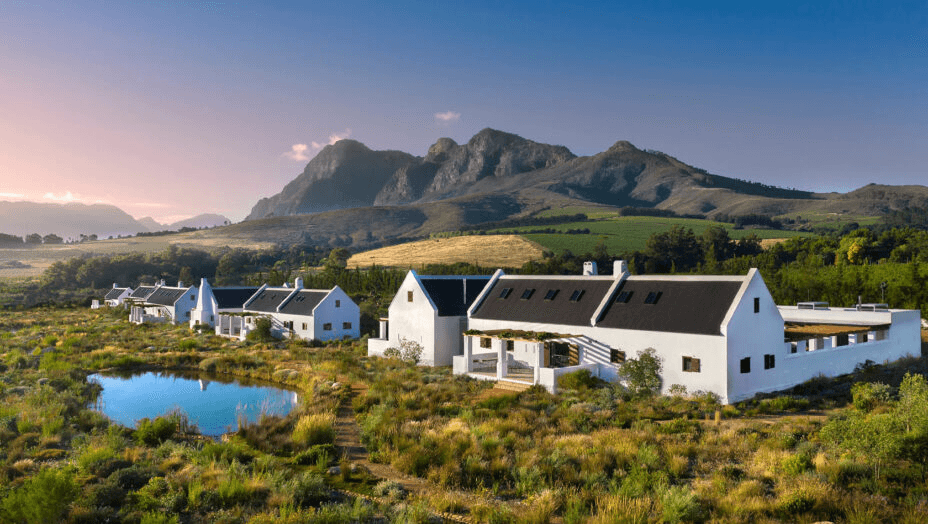 White Cape Dutch farm buildings among gardens below mountains