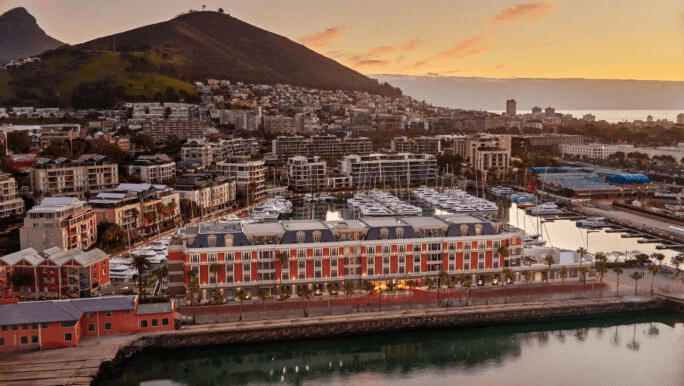 Waterfront hotel beside a marina, with mountains behind at sunset