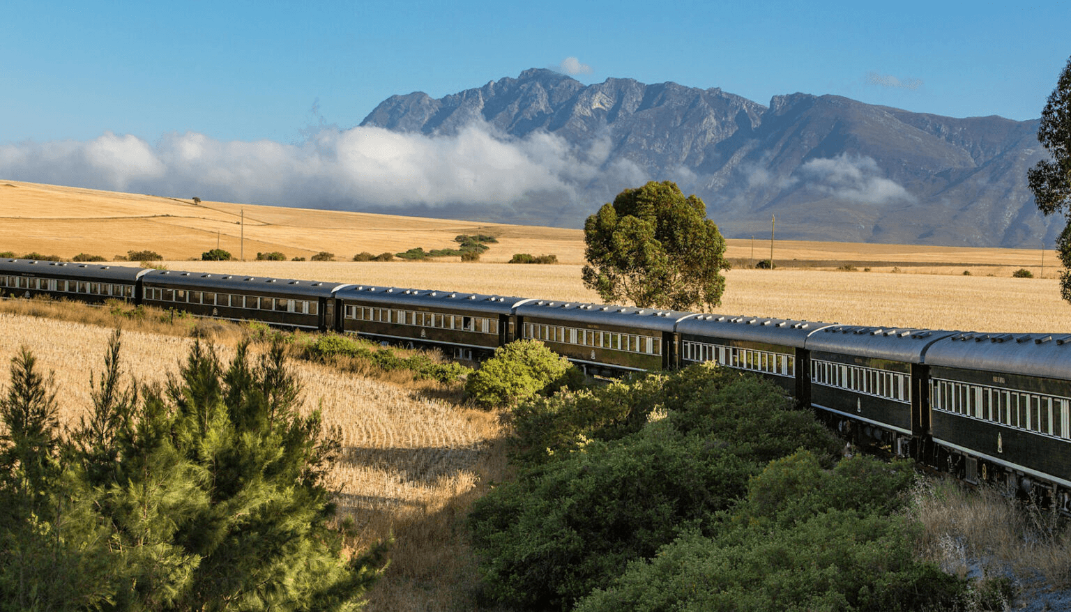 Vintage train crossing a golden plain below mountains