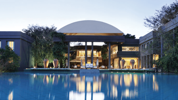 Lit hotel pavilion reflected in a long pool at dusk