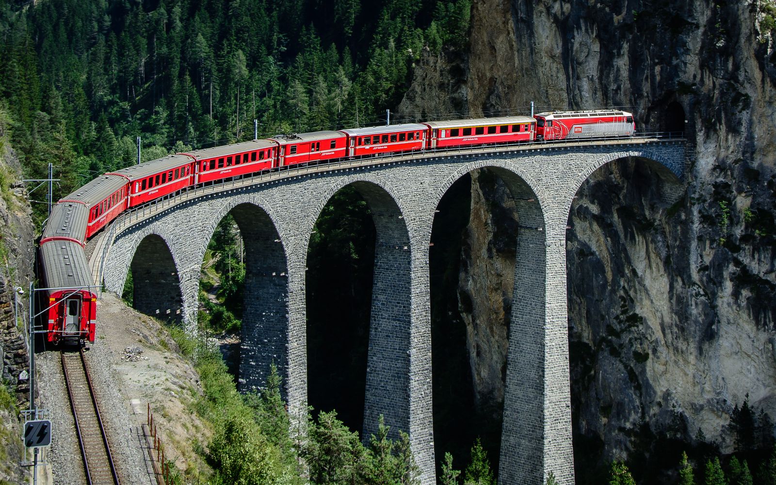Red mountain train crossing a stone viaduct
