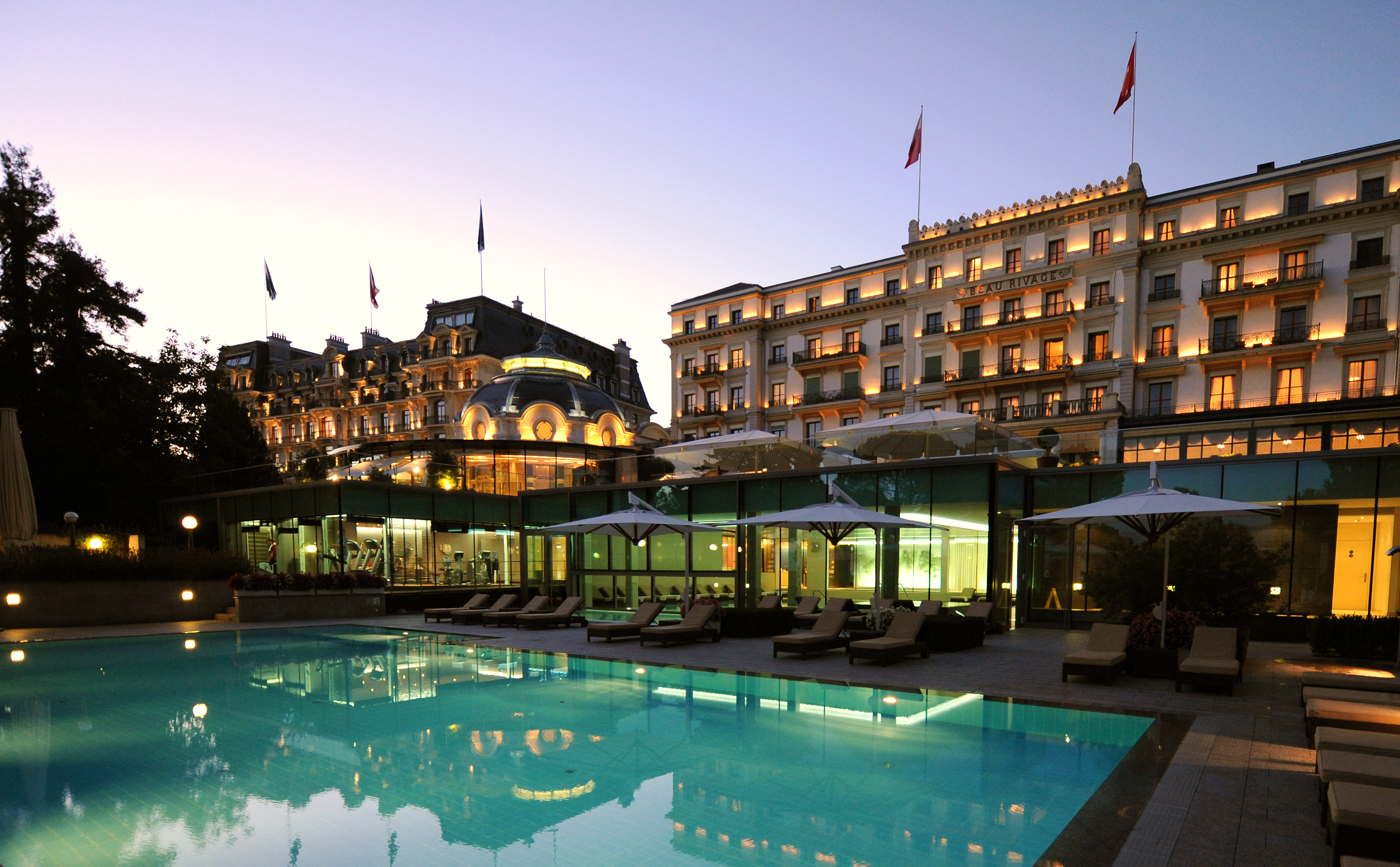 Grand hotel lit at dusk behind an outdoor pool