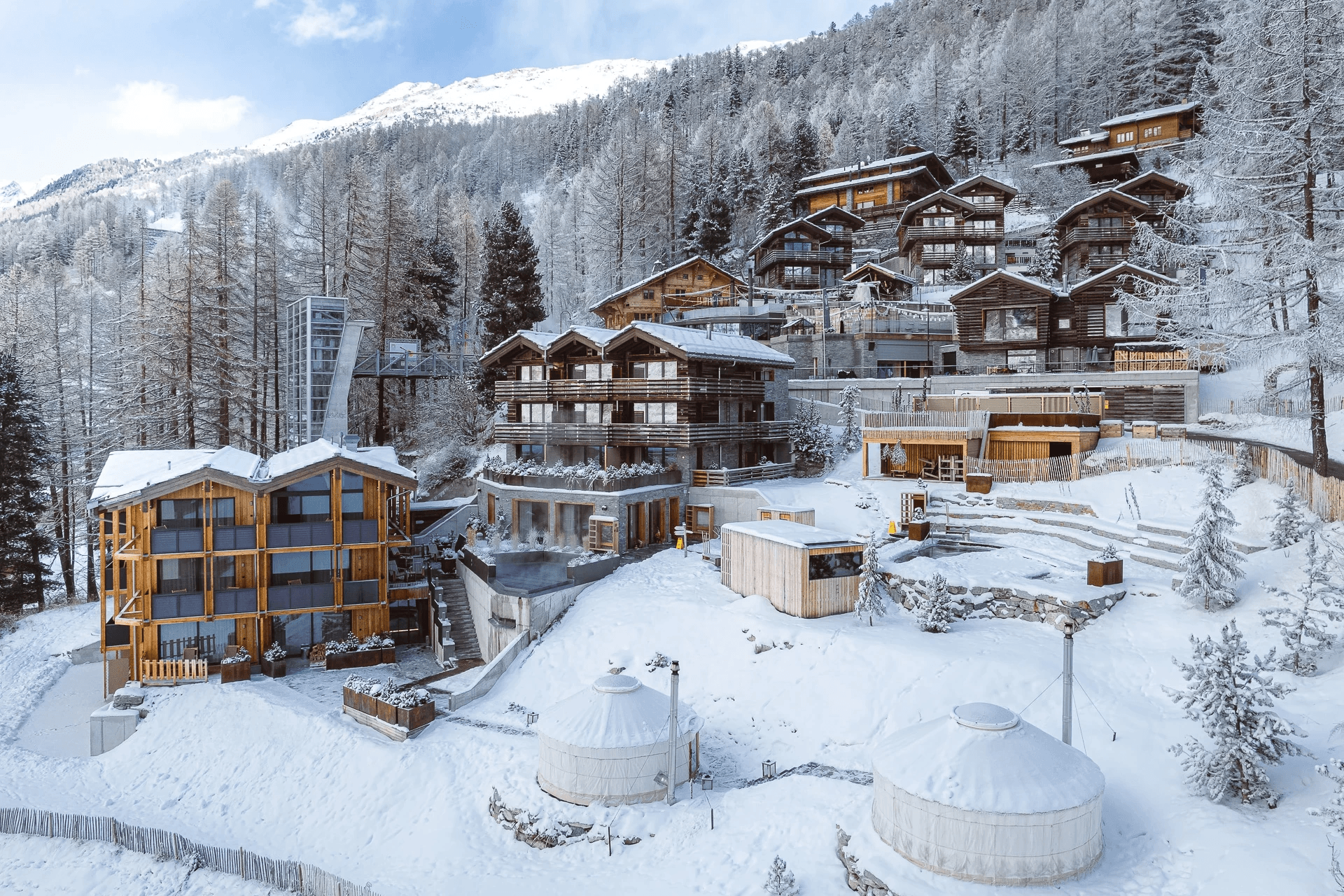 Wooden chalets on a snowy slope among larch trees