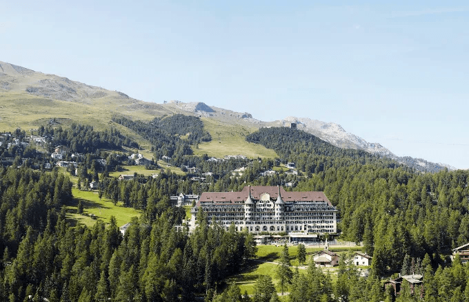 Grand hotel in a green valley below wooded slopes