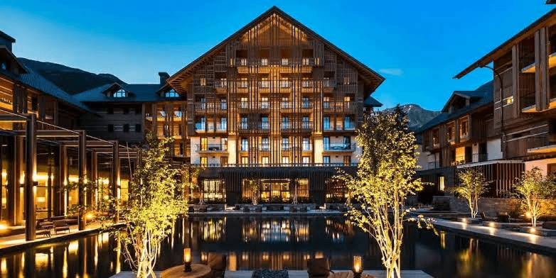 Timber hotel lit at dusk beside a reflecting pool