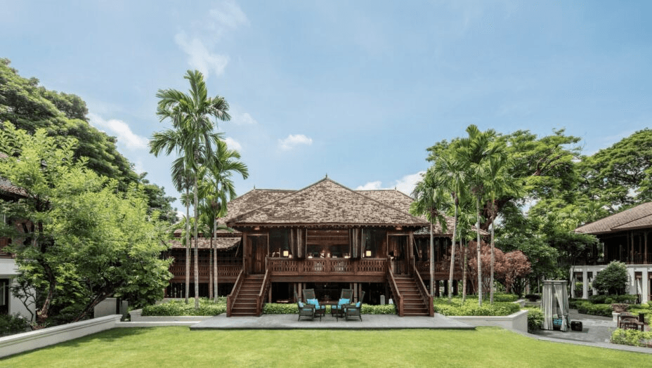 Teak colonial house on stilts beside a lawn and palms