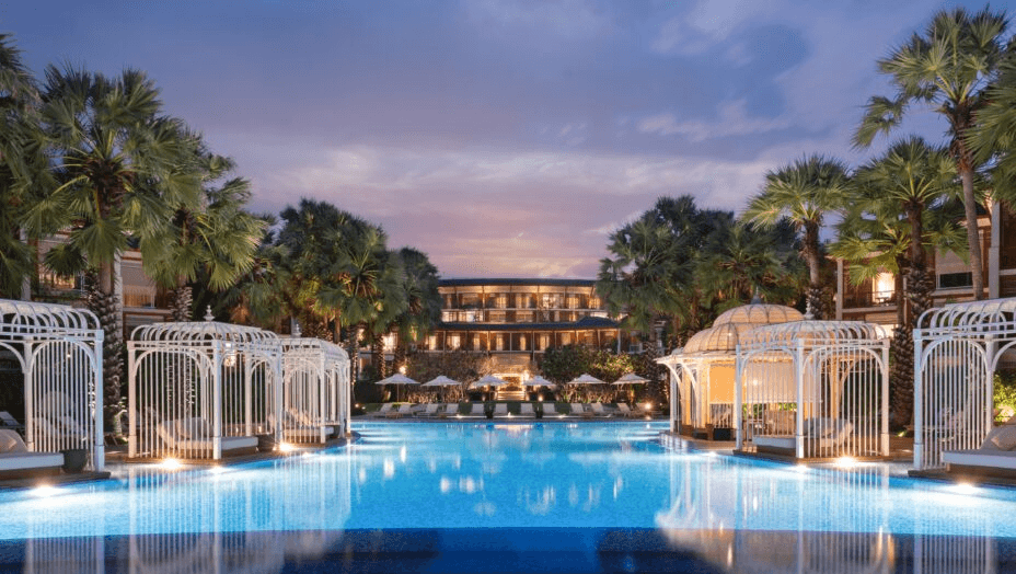 Pool flanked by white cabanas, lit at dusk