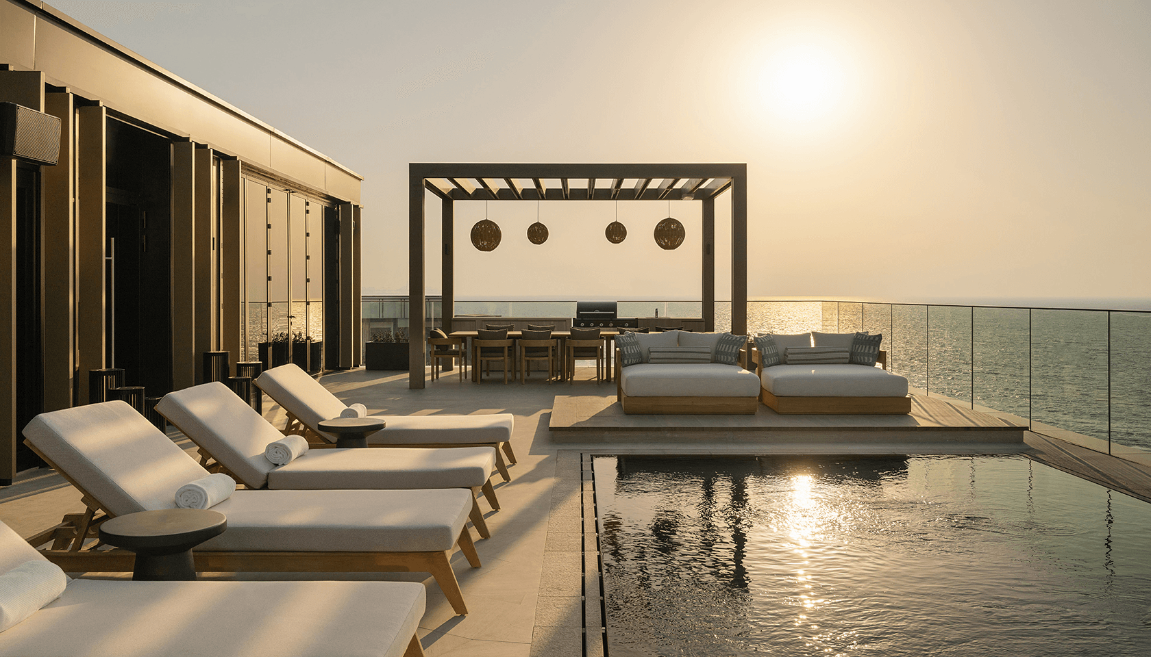 Terrace loungers beside a pool facing the sea at sunset